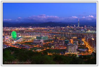 遠方的 Taipei 101、山腳的美麗華摩天輪、麥帥一橋、麥帥二橋，開始替城市點亮色彩。大直的街道與中間的松山機場的飛機，也開始忙碌起來。